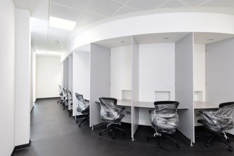 Set of white booths, each with a desk and a black desk chair - still wrapped in cellophane